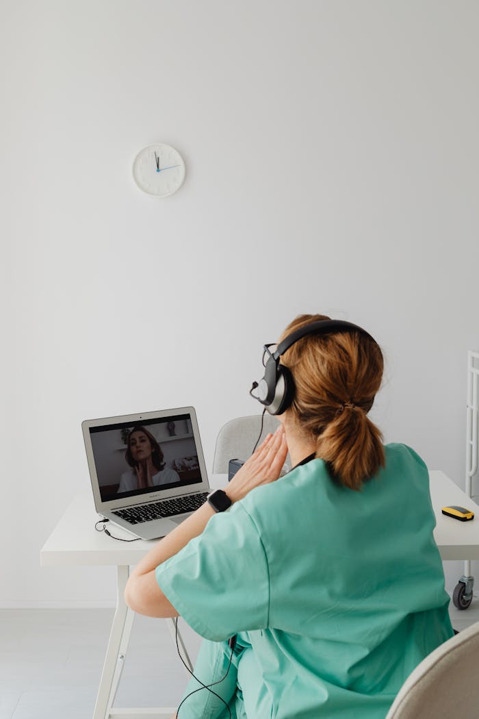 A female doctor in a green uniform conducts an online consultation through a laptop in a bright office.